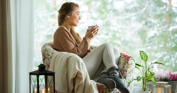 Person relaxing on a sofa with a blanket and a warm drink